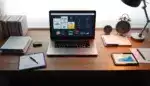 Escritorio moderno con laptop y gráficos coloridos, documentos organizados y reloj mecánico en oficina eficiente y automatizada.